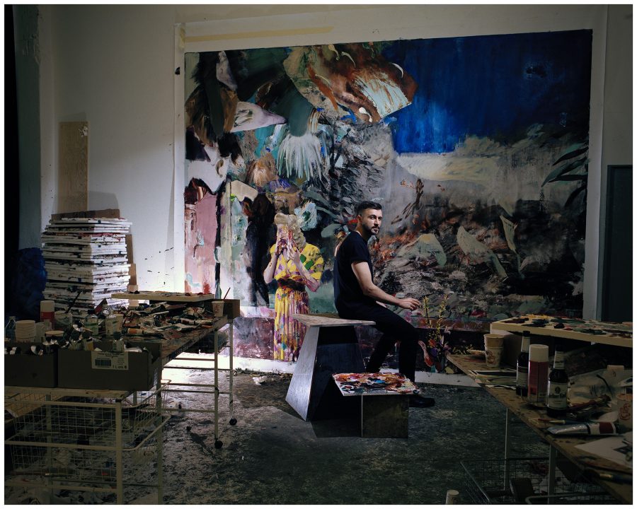 Adrian Ghenie sitting in his studio full of canvasses and painting utensils.