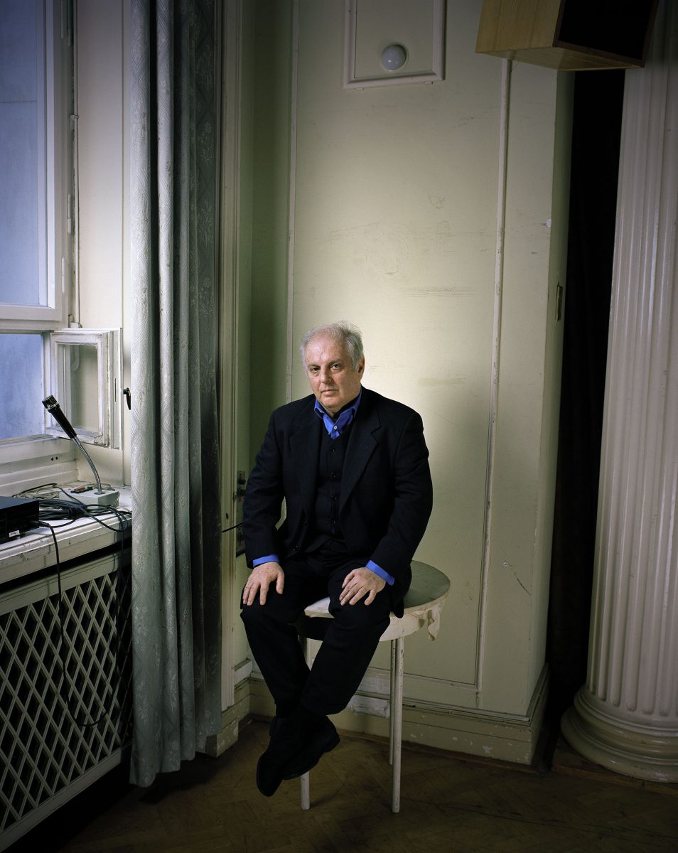 Conductor Daniel Barenboim in a black suit with blue shirt is sitting on a round side table.