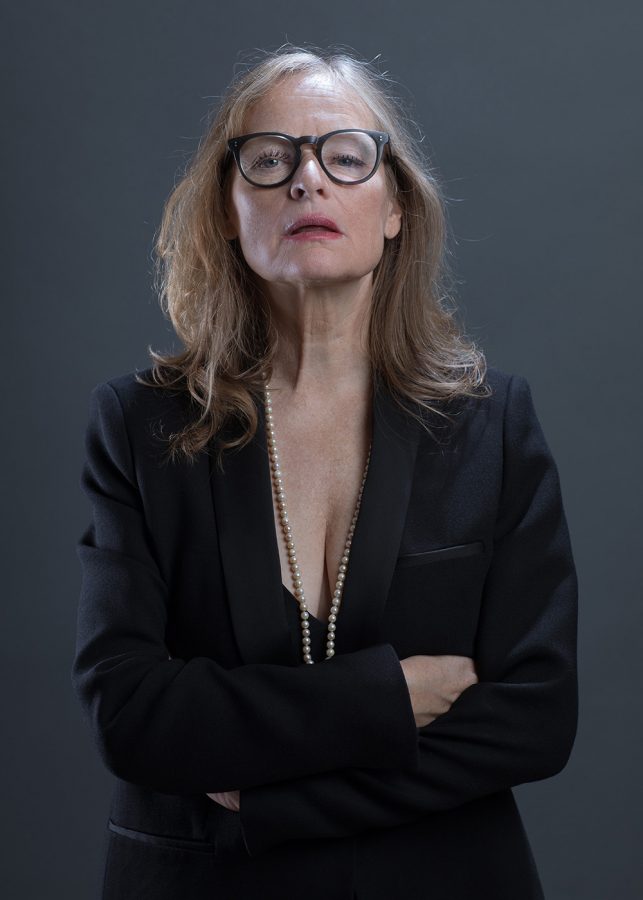 Gabi Herz wearing a pearl necklace, round glasses, and a black suit with décolleté.