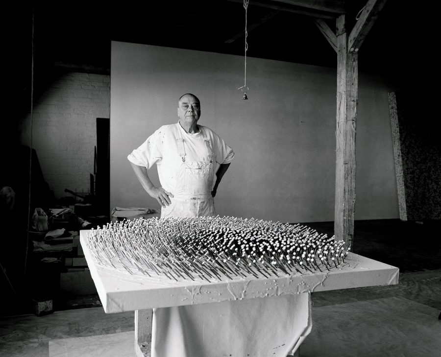 Günther Uecker standing with one of his nail sculptures.
