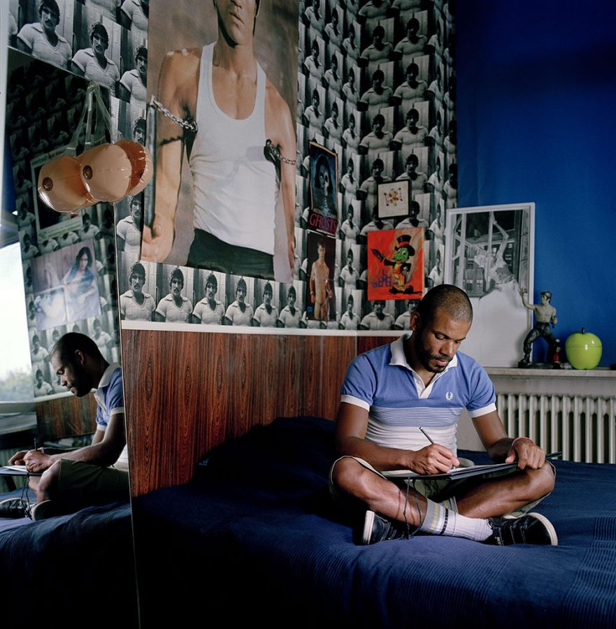 Marc Brandenburg sitting in his bedroom with photos, art, and decorations on the walls.