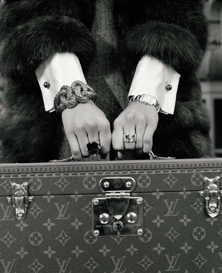 two hands with expensive jewelry hold a Louis Vuitton jewelry case.