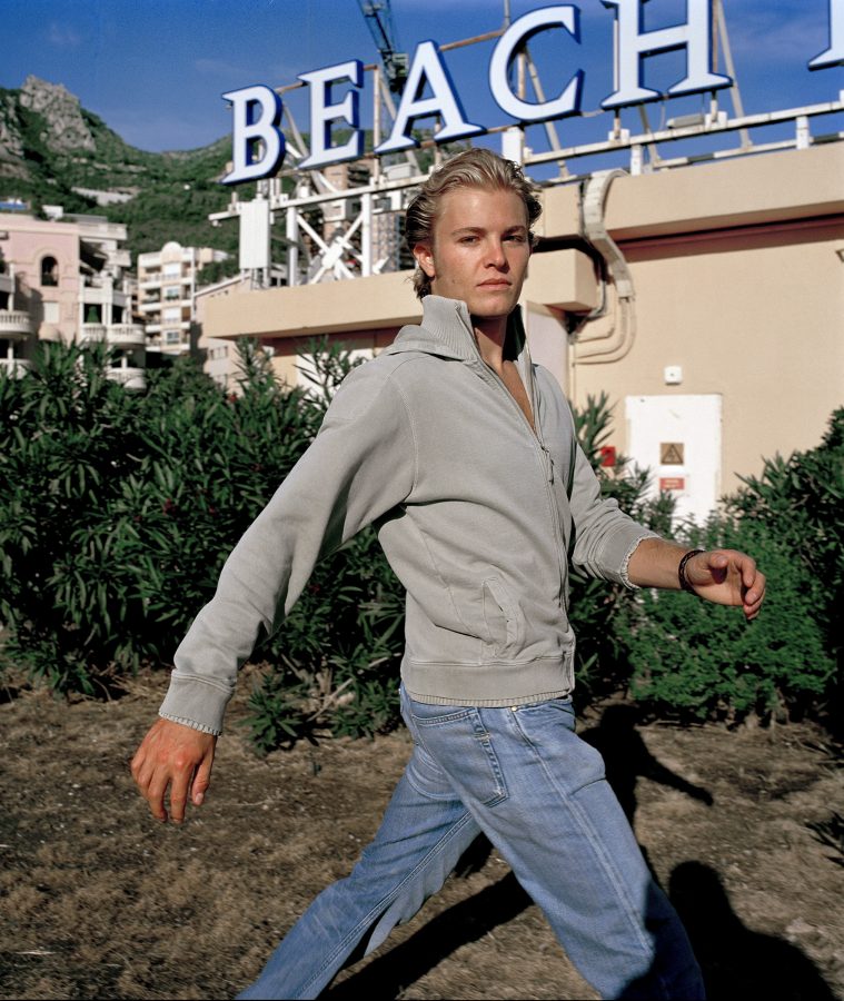 Racing driver Nico Rosberg in jeans walking on a rooftop. The house behind him carries a partially visible sign that reads „Beach“.