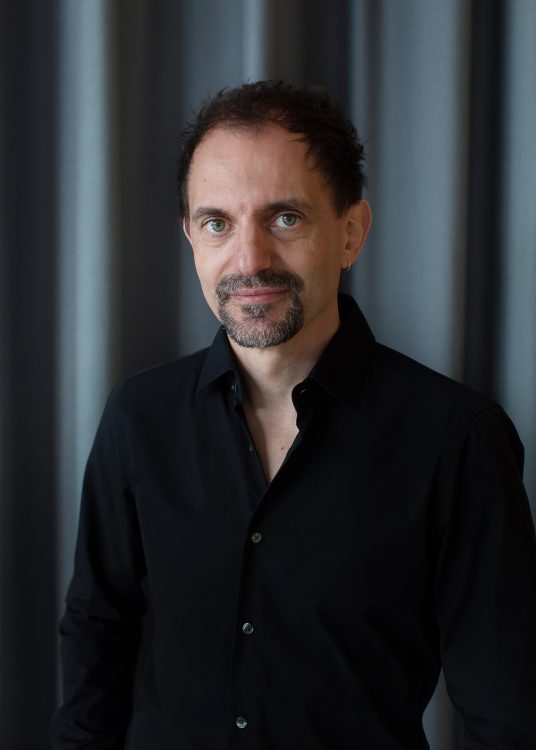 The artistic director of the Ruhr Festival Olaf Kröck wearing a black shirt in front of a curtain.