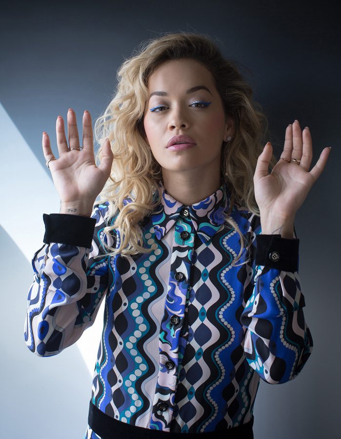 Rita Ora in a shirt with abstract pattern. She is holding her hands in the air.