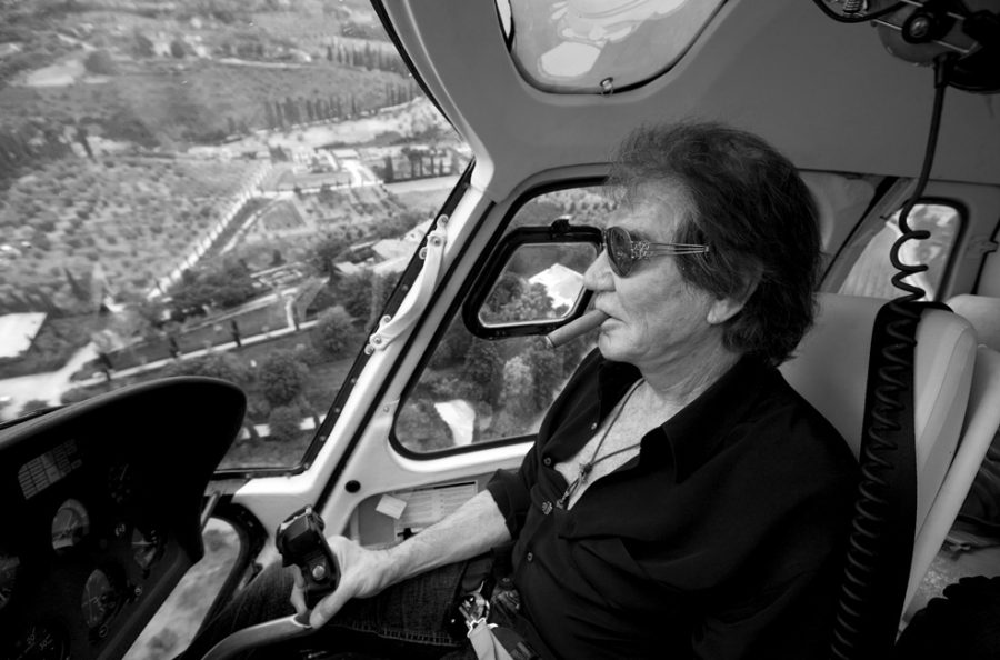 Roberto Cavalli piloting his helicopter over Italian landscapes with cigar in mouth.