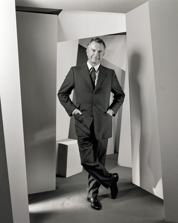 Actor Sam Neill wearing a large, old-fashioned suit with a smile on his face.