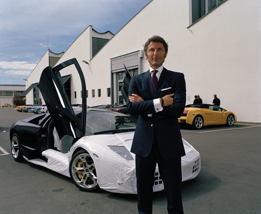Stephan Winkelmann with arms crossed standing in a parking lot with Lamborghinis.