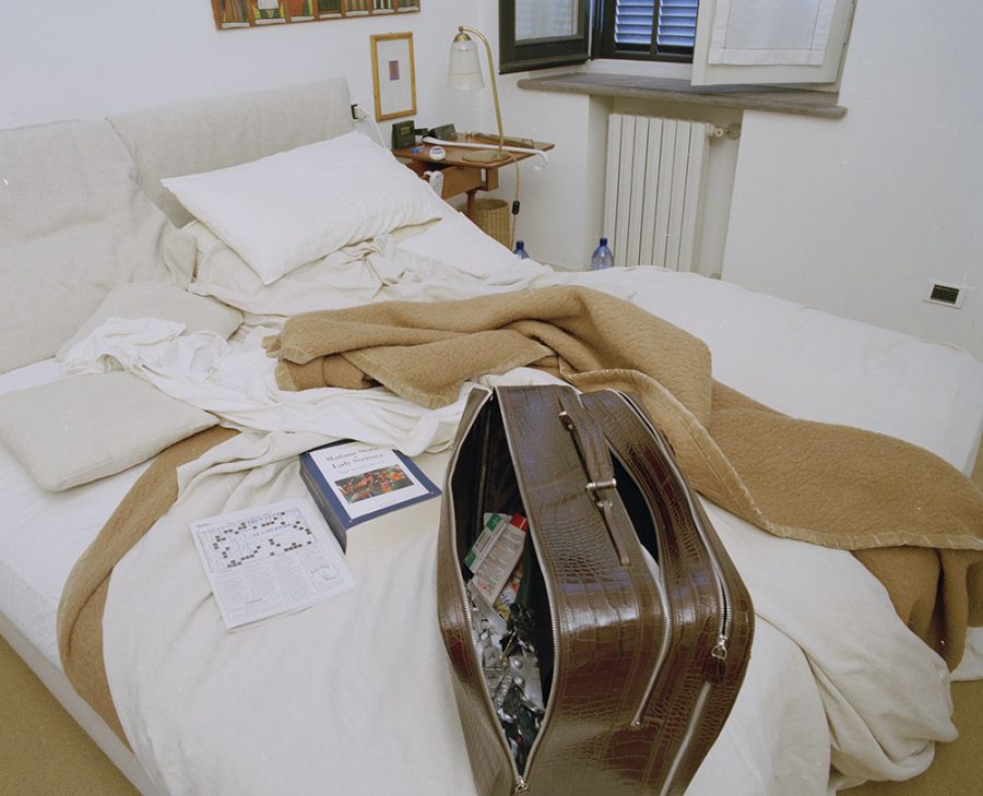 Unmade bed with a stuffed suitcase and books on top of it.