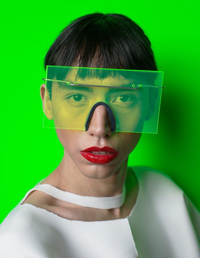 Agustin Noguera wearing red lipstick in front of a bright, green background.