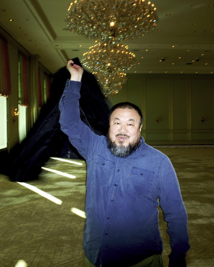 Ai Weiwei waving his jacket through the air in a room with chandelier.