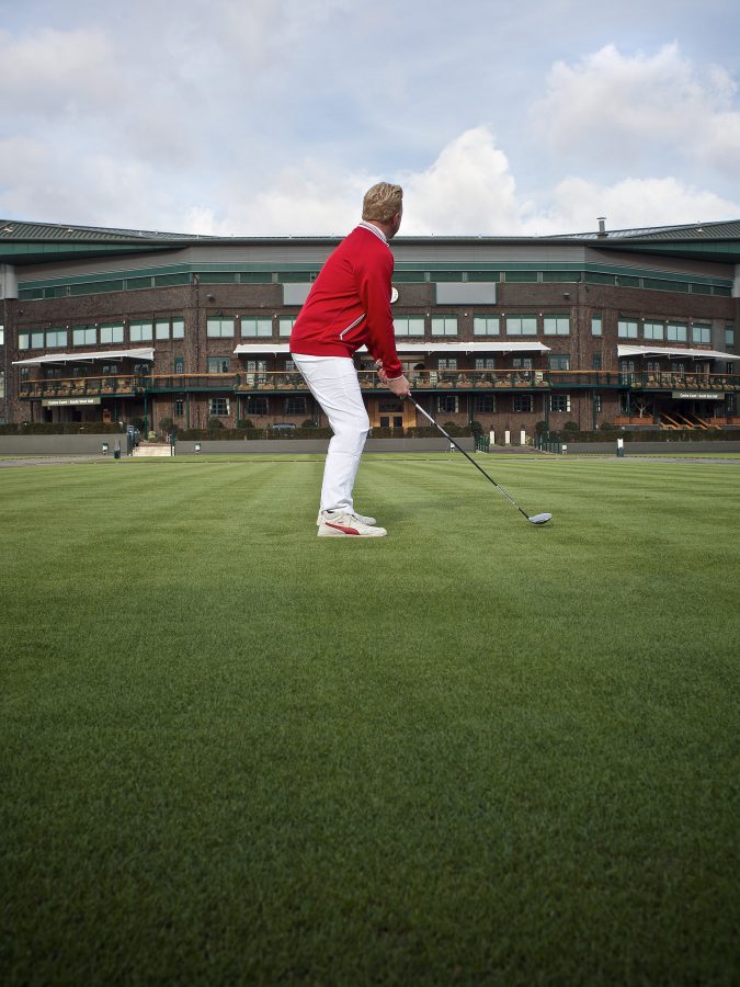 Boris Becker standing on green grass is about to swing is golf club.