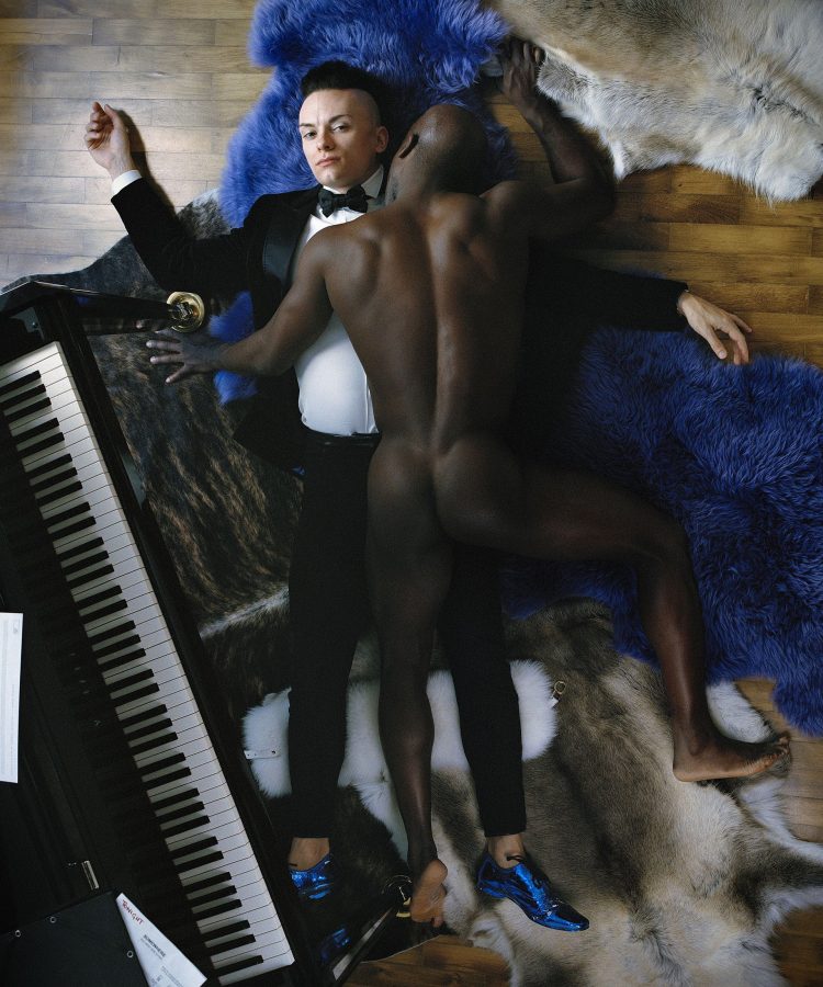 Top view of Cameron Carpenter and his nude personal trainer laying on colorful carpets next to a piano.