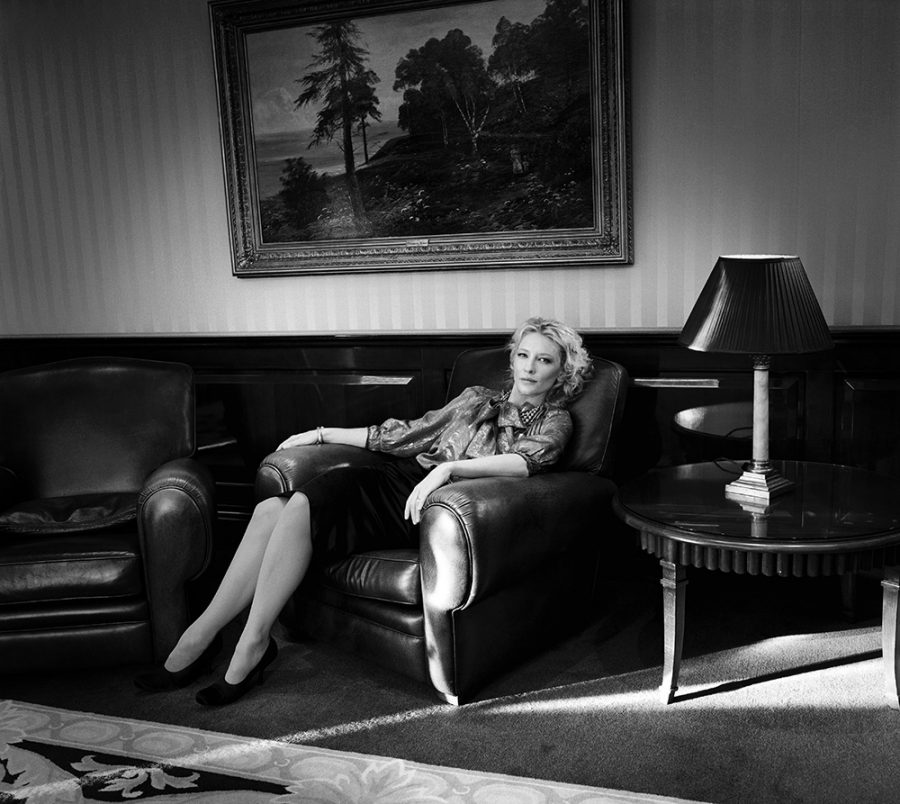 Cate Blanchett posing for a photo in an elegant outfit on a hotel lobby couch.