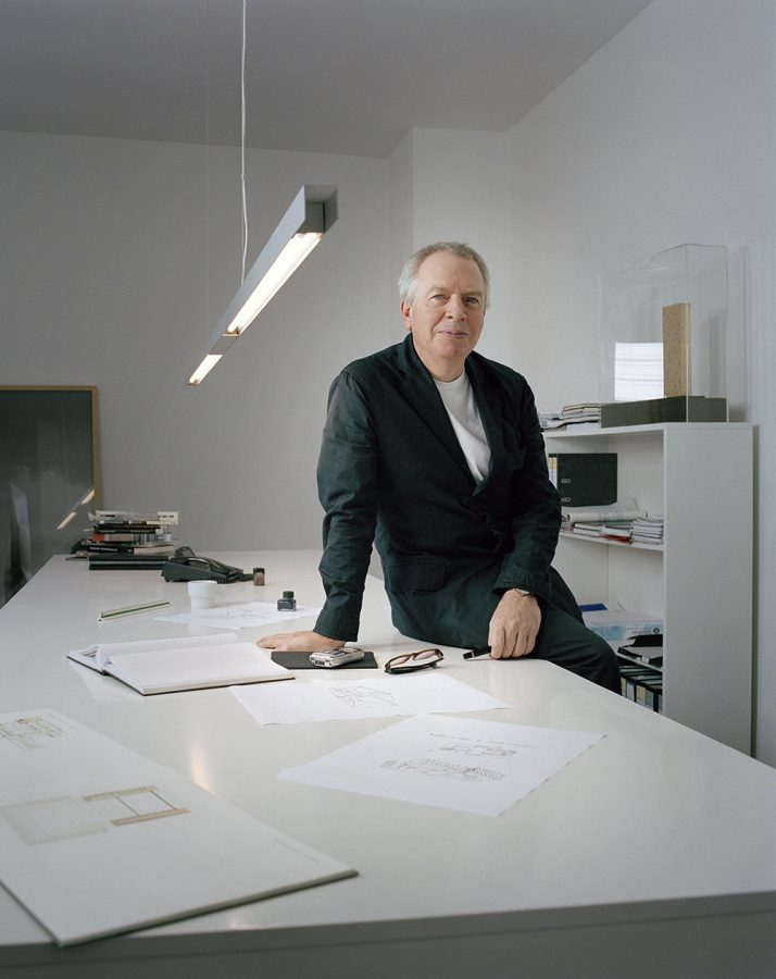 David Chipperfield in his office leaning on a white table.