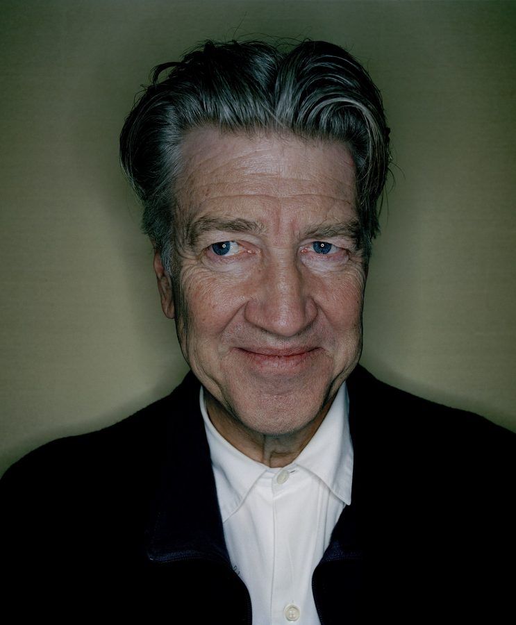 Portrait of a smiling David Lynch in a black suit and white shirt.