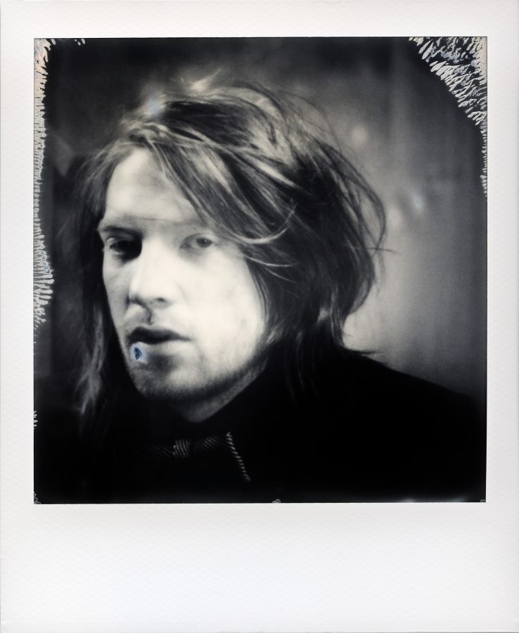 Black and white Polaroid photo of Irish actor Domhnall Gleeson with long hair.
