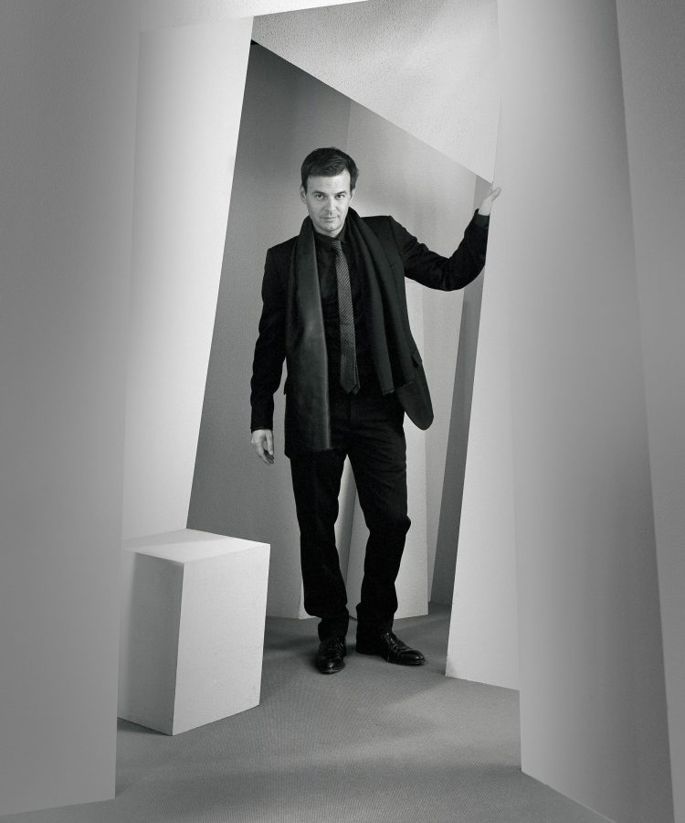 François Ozon wearing a black suit in a white room.