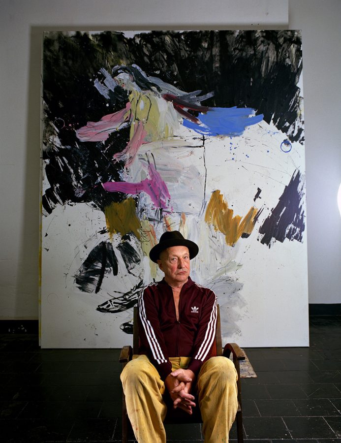 Georg Baselitz in an Adidas tracksuit sitting in front of painting.