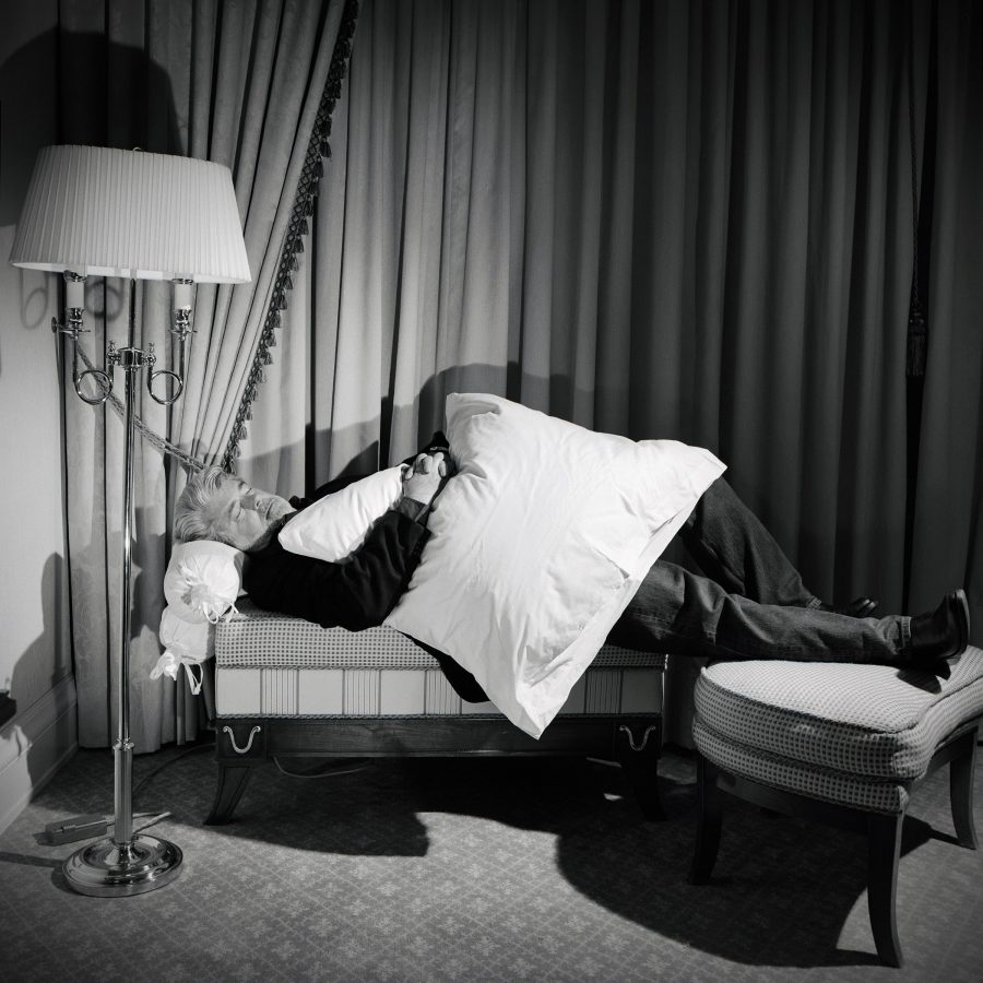 George Lucas lying on a sofa in hotel room with a pillow on his lap.