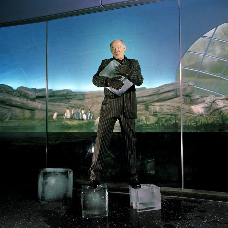 Hans Joachim Schellnhuber in a black pinstripe suit posing for the camera on two large melting ice cubes in a science museum.