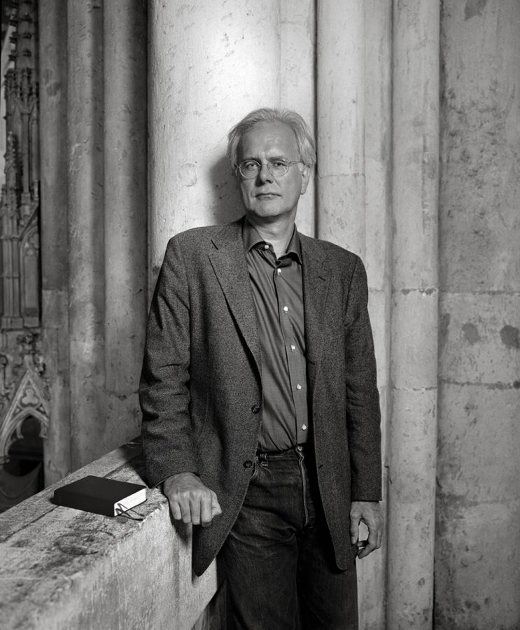 Harald Schmidt leaning against wall with a book beside him.