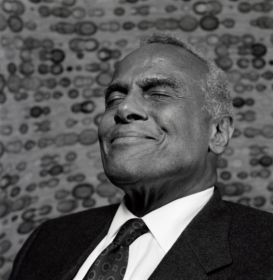 Harry Belafonte in a suit enjoying the sunshine with a smile on his face.