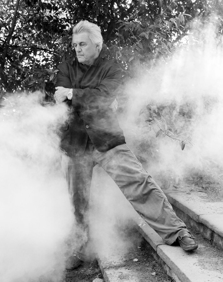 Novelist John Irving crossing his arms surrounded by smoke.