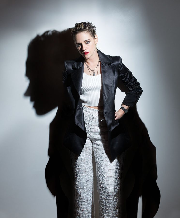 Full-frontal portrait of Kristen Stewart casting shadow on a white wall.