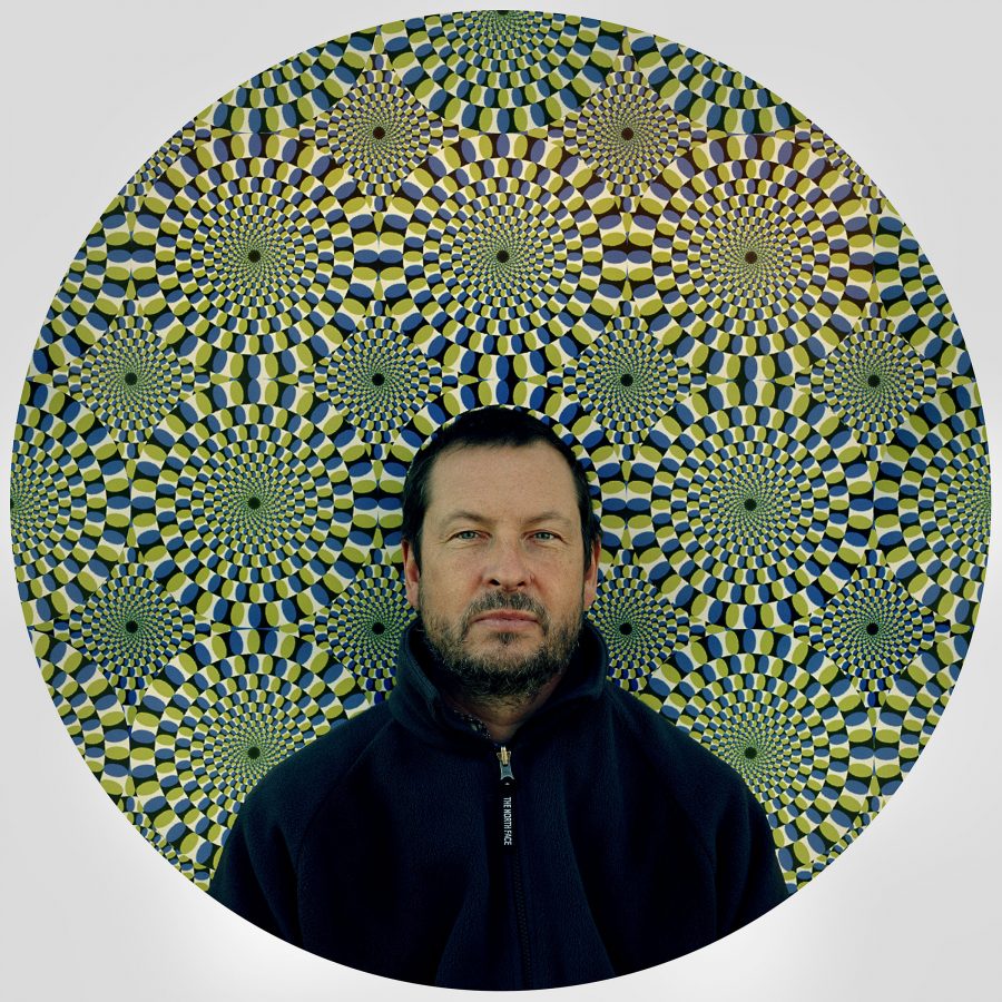 Lars von Trier posing for a portrait in front of a spinning wheel optical illusion.