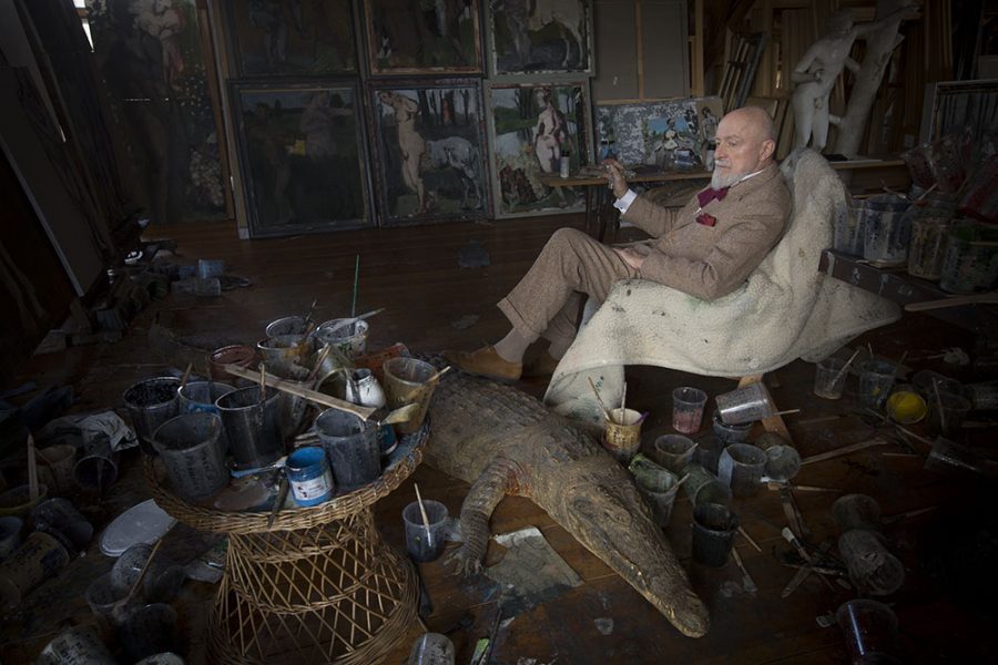 Markus Lüpertz sitting in his cluttered atelier with a crocodile dummy on the wooden floor.
