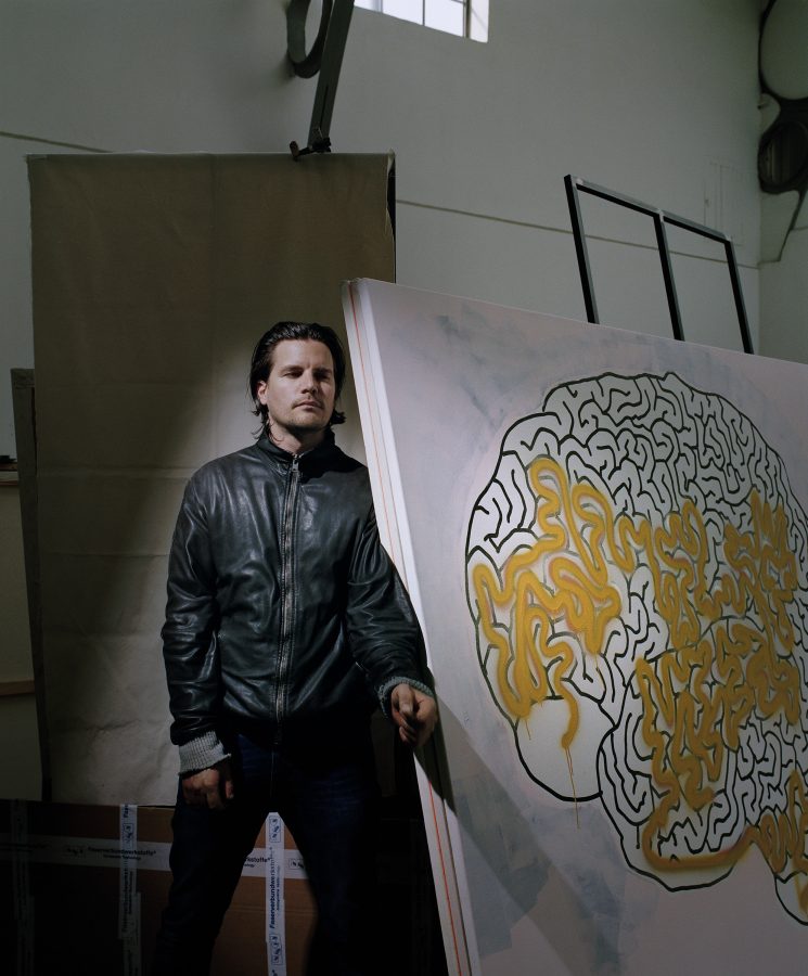 Artist Michael Sailstorfer in his studio next to a painting of a brain.