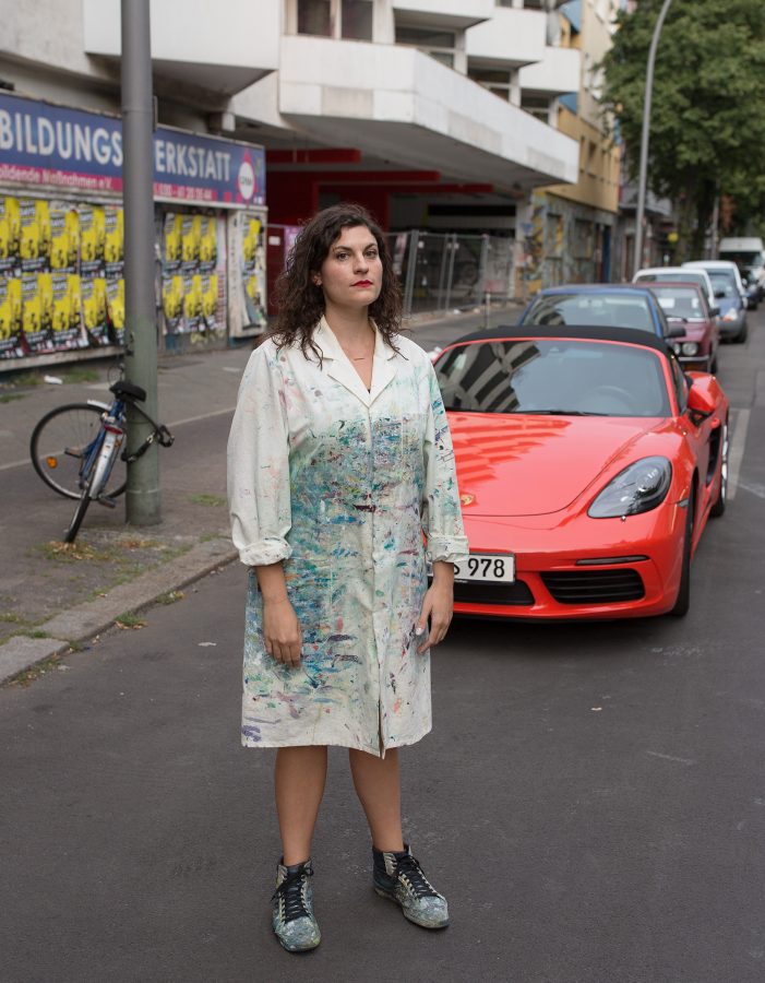 Michelle Jezierski wearing a painter coat on a street in front of a red Ferrari.