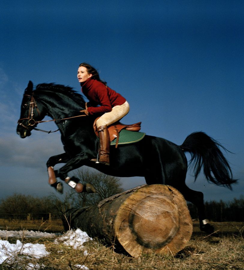 Nadeshda Brennicke on the back of a black stallion jumping over a log.