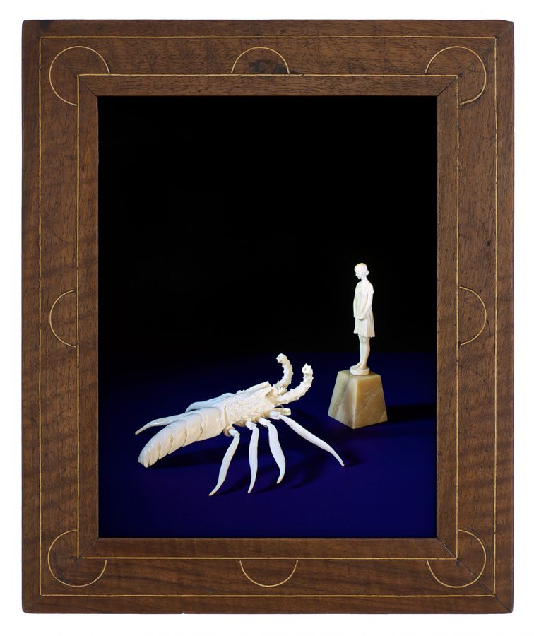 Photo of two ivory carvings of a scorpion and a woman in a historical frame.