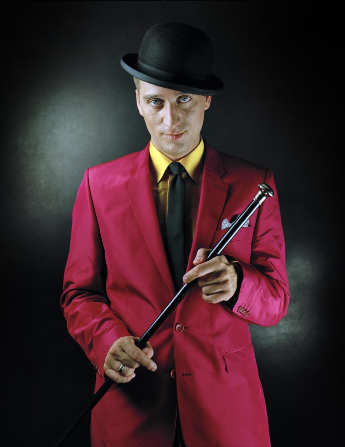 Paul Van Dyk wearing pink suit, yellow shirt, top hat and a walking stick.