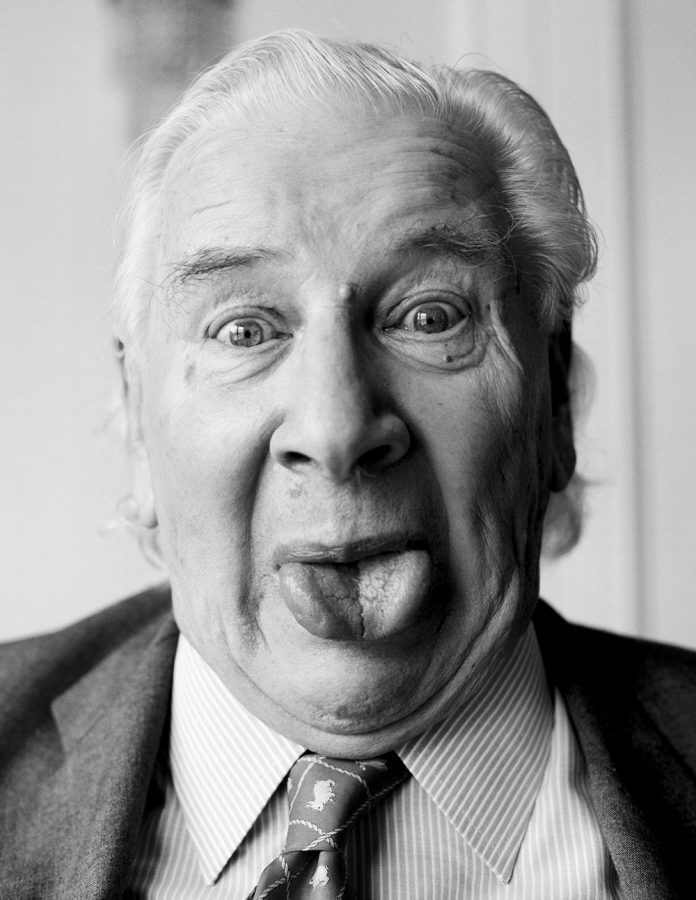 Portrat of Peter Ustinov sticking out his tongue. He is staring directly into the camera.