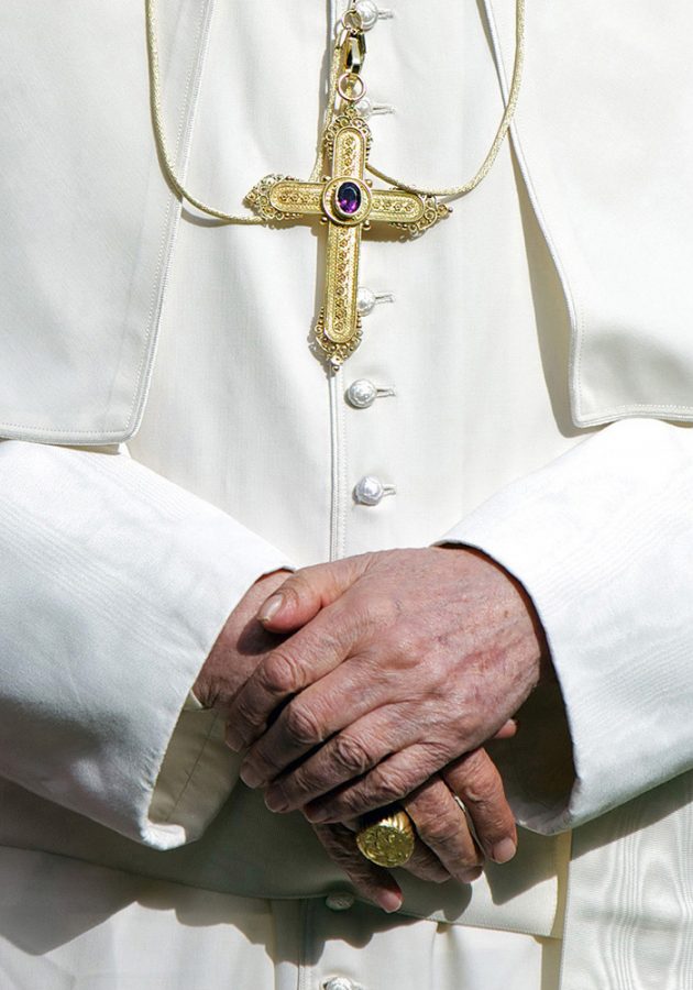 Close-up portrait of Pope Benedict's clasped hands. The pope is wearing a white gown, a golden ring and a crucifix.