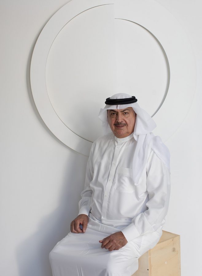 Rashid bin Khalifa Al Khalifa seated on wooden boxes in front of one of his artworks.