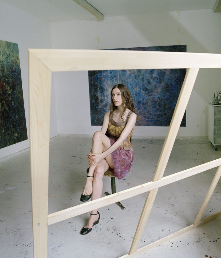 Sibylle Springer in her sparse atelier with two paintings haning on the wall.