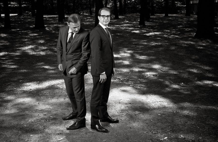 Thomas Oppermann and Alexander Dobrindt in suits standing back to back in a forest.