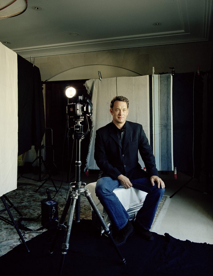 Tom Hanks wearing black jacket and jeans posing for the camera in a photography setup.